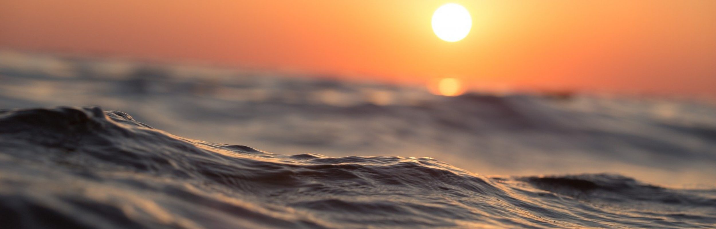 sun setting over the ocean with a glowing orange sky